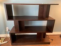 Front view of a dark brown wooden shelving unit with four staggered shelves against a light blue wall.