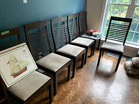 Six wooden Nordic style dining chairs lined up against a blue wall, showing overall condition and setup.