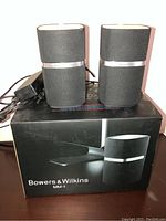 Pair of Bowers & Wilkins MM-1 speakers on top of the product box, with power adapter and cables visible.