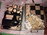 Two wall art pieces, one with fruit in a black vase and the other with a floral leaf motif and checkered pattern.
