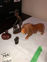 Photo showing four wood carvings on white cloth, including a lion, a figure holding an animal, and two head carvings.