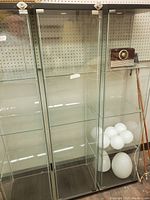 Full view of the tall glass display cabinet with multiple clear glass shelves and metal frames, showing some items inside on shelves.