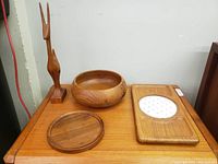 Photo of the teak sculpture, bowl, round board, and rectangular board on a wooden surface.