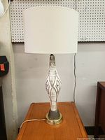 Front view of vintage Mid-Century Modern ceramic table lamp showing white ceramic base with gray geometric patterns, brass metal base, and white fabric drum shade.