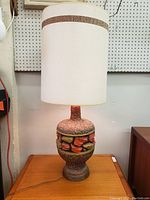 Full view of the vintage ceramic table lamp with textured surface and white shade on wooden surface.