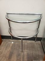 Front view of vintage chrome console table showing curved glass top and tubular frame.
