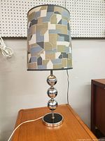 Full lamp showing chrome base with three polished spheres and tall patterned fabric lampshade on wooden surface.