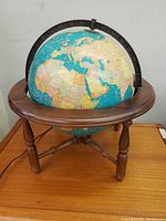 Front view showing the globe turned off, clear view of map details on half globe, wooden legs, and metal meridian ring.