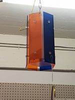 Front and slightly side view of the orange and blue hanging light fixture showing its hexagonal shape and translucent colored panels with fasteners.