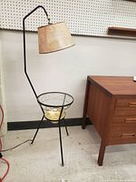 Full view of black metal floor lamp with arched arm and beige lampshade beside wooden cabinet