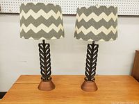 Pair of matching Mid-Century Modern table lamps with metal leaf shafts on teak bases and zigzag fabric shades, shown side by side on a surface.