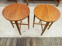 Pair of teak folding side tables front view showing round tops and cross-braced legs