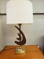 Side view of the lamp showing the full white fabric drum shade, sculptural wood centerpiece, and brass square base with cord.