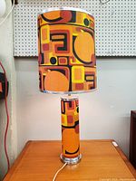 Front view of vintage table lamp showing the tall cylindrical shade and base with bright geometric pattern fabric.