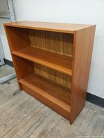 Front view of the vintage teak book stand showing three shelves with open storage.