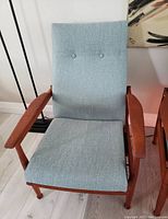 Front view of armchair showing light blue upholstery and teak frame