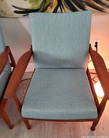 Front view of two identical teak armchairs placed side by side against a wall with abstract painting