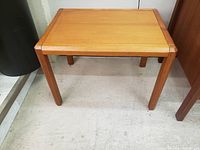 Front view of vintage teak side table showing rectangular top and tapered legs on a concrete floor.