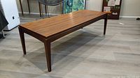 Photo showing side view of rectangular walnut coffee table with tapered legs on laminate flooring.