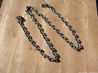 Steel chain lying flat on wooden surface, showing full length and both ends with hooks.