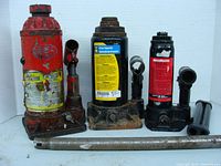 Three hydraulic bottle jacks with pump handles placed in front, showing all items in the lot.