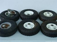 Four sets of used dolly wheels arranged showing both white and rusted metal hubs with rubber tires.