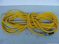 Photo shows a yellow 50-foot 12 gauge extension cord coiled on a flat surface. Both plug ends visible: male three-prong plug and female socket with protective cover.