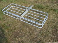 Aluminum cargo carrier made of tubular aluminum with a hitch mount and rectangular platform design lying on grass.