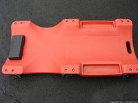 Top side view showing orange plastic surface with foam headrest and carry handle.