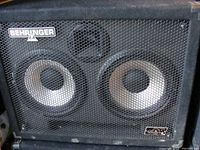 Front view of one Behringer Ultrabass BA210 speaker showing dual 10-inch woofers behind metal grille with Behringer branding and logo.