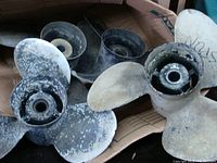 Box containing multiple metal boat propellers with visible corrosion and use marks, for Alpha One drives.