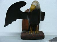 Front view of carved wooden eagle with one wing attached and one wing missing, mounted on wooden backplate.