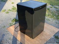 Photo of black Danby Millennium mini refrigerator with visible power cord, exterior shows minor cosmetic wear.