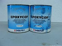 Two metal cans of Interlux Epoxycop Nautical K51 Blue Marine Bottom Paint, one full and one partially used, showing front labels with branding and product details.