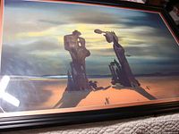 Full view of the large framed surrealist style print showing two tall abstract figures on a beach with shadows and a moody sky.