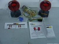 Two red round magnetic trailer lights on black magnetic bases with wiring harness, wire connectors, and instruction manual laid out on a grey surface.
