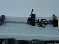 Full side view of the trolling motor laid on a table showing the motor housing, shaft and propeller.