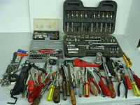 Wide view of all miscellaneous hand tools displayed including various pliers, screwdrivers, socket sets in cases, wrenches, clamps, and other tools spread on a surface.