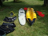 All contents laid out on grass: deflated floor board, kayak tubes, two backrest seats, pump and paddles