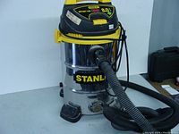 Full front view of the Stanley wet/dry shop vacuum showing stainless steel container, black and yellow top housing with vacuum hose attached.