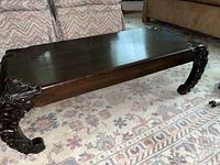 Full view of a rectangular solid wood coffee table with carved legs, showing dark wood surface and overall build.