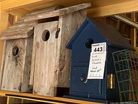 Wooden and blue painted bird houses, each with a circular entrance hole, displayed on a shelf.