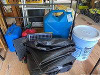 Overview photo showing the three containers: blue gasoline, red kerosene, and large blue water container, along with a white bucket, black tarps, and a small solar panel.