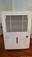 Front view of white Frigidaire dehumidifier showing air intake grille, water level indicator, and overall unit front.