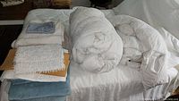 Two rolled white down comforters, folded blankets and towels on bed