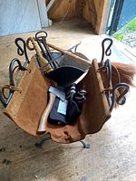 Photo showing close-up front view of fireplace tools including shovel and poker with looped wrought iron handles, natural bristle brooms, leather log holder set in wrought iron folding base, and metal bucket.
