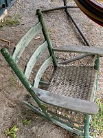 Antique green wooden rocking chair showing the damaged woven seat and weathered paint.