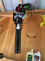 Full view of the EGO cordless leaf blower with battery attached, charger plugged in, and 3M noise reducing headphones hung over blower handle.