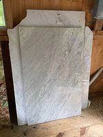 Two white Carrera marble slabs leaning against a wooden wall, one smaller rectangular tabletop and one larger slab visible.