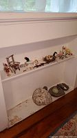 Wide shot of shelf with wooden, metal, porcelain figurines and assorted stones including large quartz and stone egg below shelf.